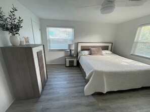 A bedroom with a bed, bedside table, lamp, and a dresser. - Cedar By The Sea - steps to the beach/Flagler Ave (New Smyrna Beach)
