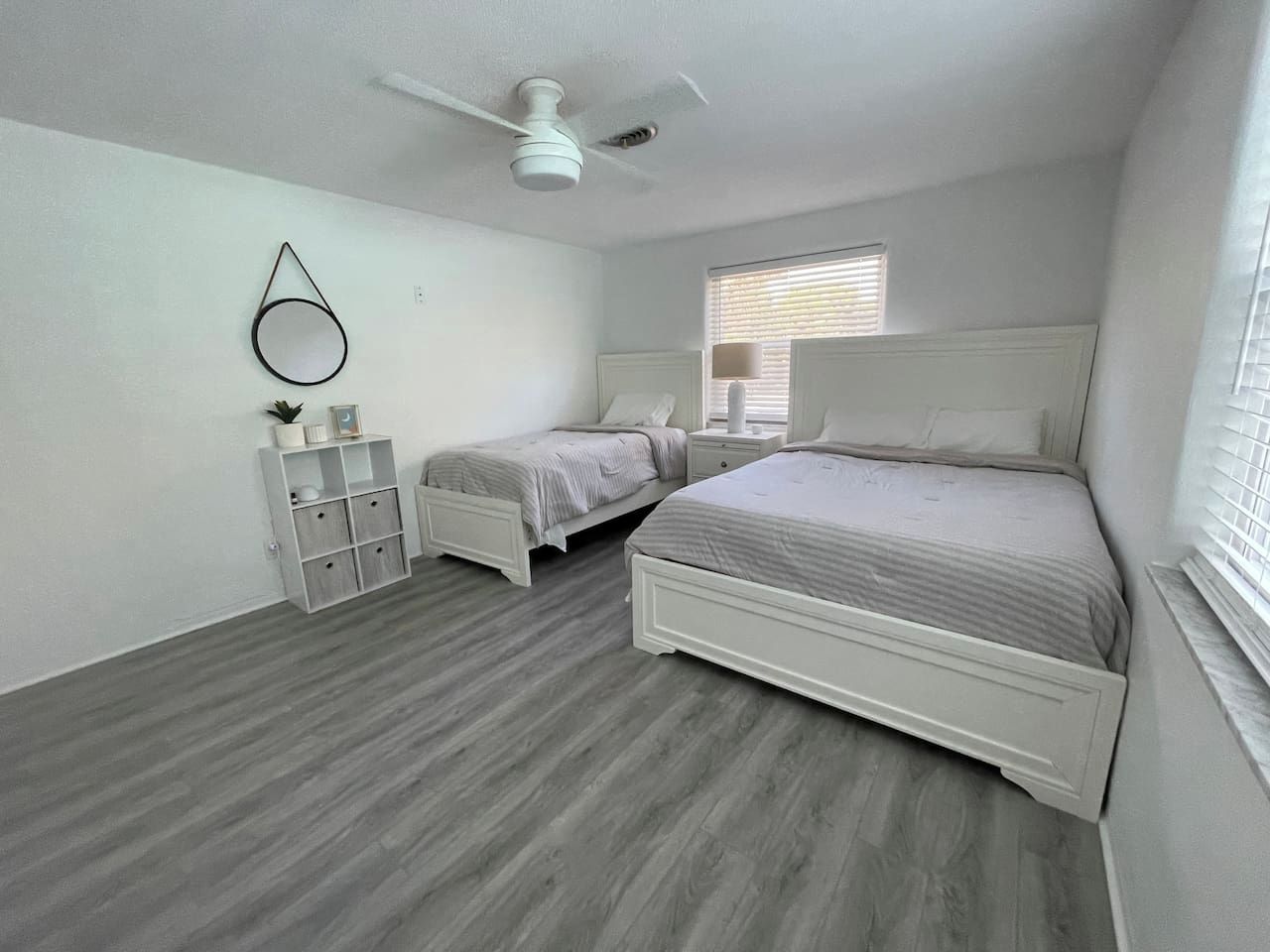 A bedroom with two beds, a ceiling fan, a window with blinds, and a white wardrobe.