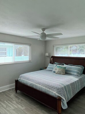 A bedroom with a bed, a ceiling fan, and two windows with blinds. - Sandy Toes on Cedar - steps from the beach (New Smyrna Beach)