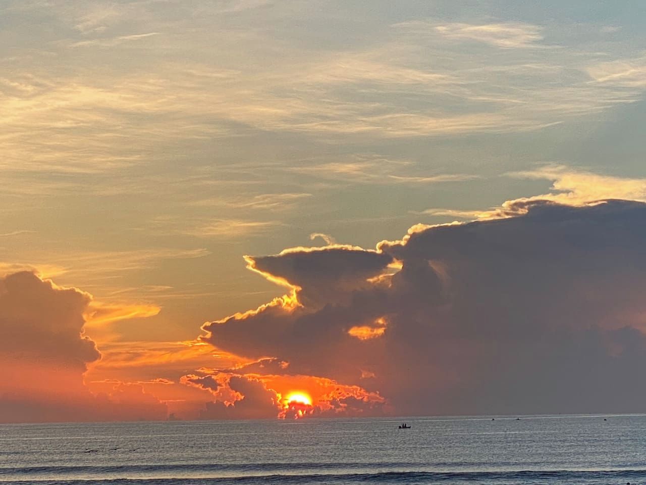 Pôr do sol sobre o oceano com nuvens e o horizonte de uma cidade distante.