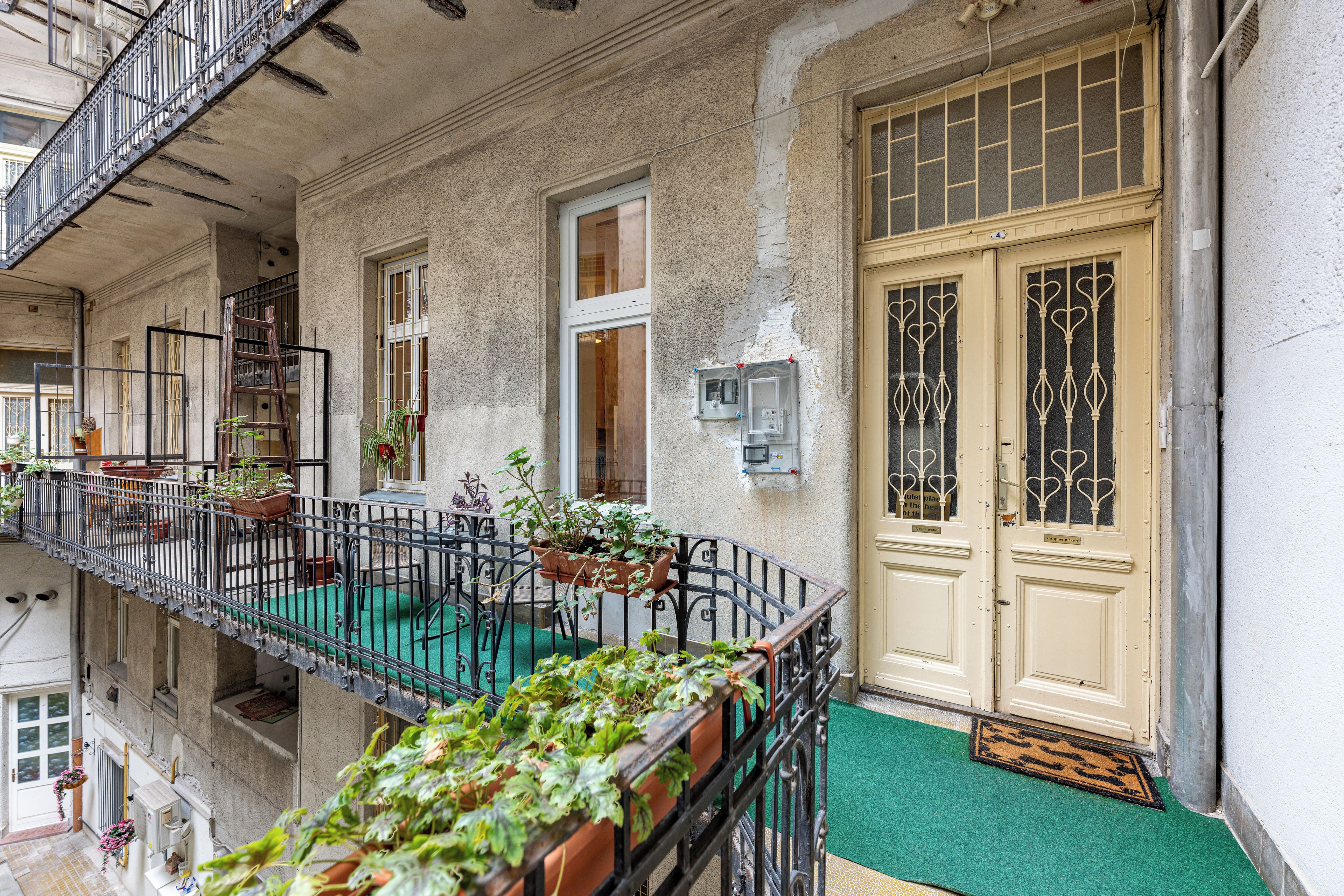 Un edificio con un balcone, piante in vaso e una porta con un cartello.