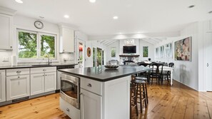 A modern kitchen with white cabinetry, a large island, and a dining area with wooden flooring. - Updated Montauk retreat with breathtaking ocean views and effortless... (Montauk)