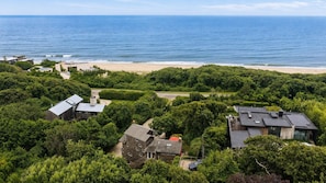 Un quartier résidentiel situé sur la côte, avec des maisons entourées d’une végétation luxuriante, une plage et l’océan en toile de fond.