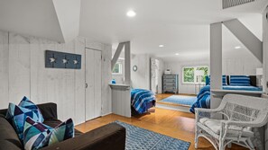 Habitación amplia con una cama grande, un sofá y una silla. Se ve un ventanal con vistas a zonas verdes.