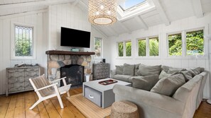 Una sala de estar acogedora con chimenea de piedra, un televisor de pantalla plana montado encima y un sofá gris junto a una silla de madera.