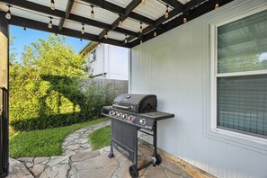 An outdoor grill area with a stone pathway leading to it, a wooden fence, and a house in the background.