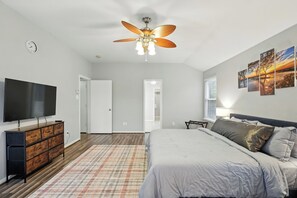 Ein Schlafzimmer mit einem Bett, einem Fernseher, einer Kommode, einem Deckenventilator und einem Fenster mit Jalousien.
