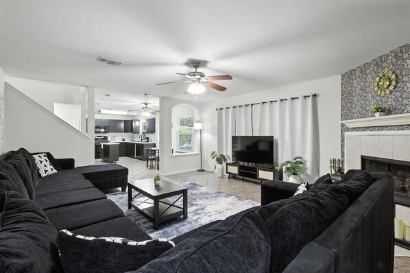 A modern living room with a sectional sofa, a coffee table, a flat-screen TV, and a fireplace.