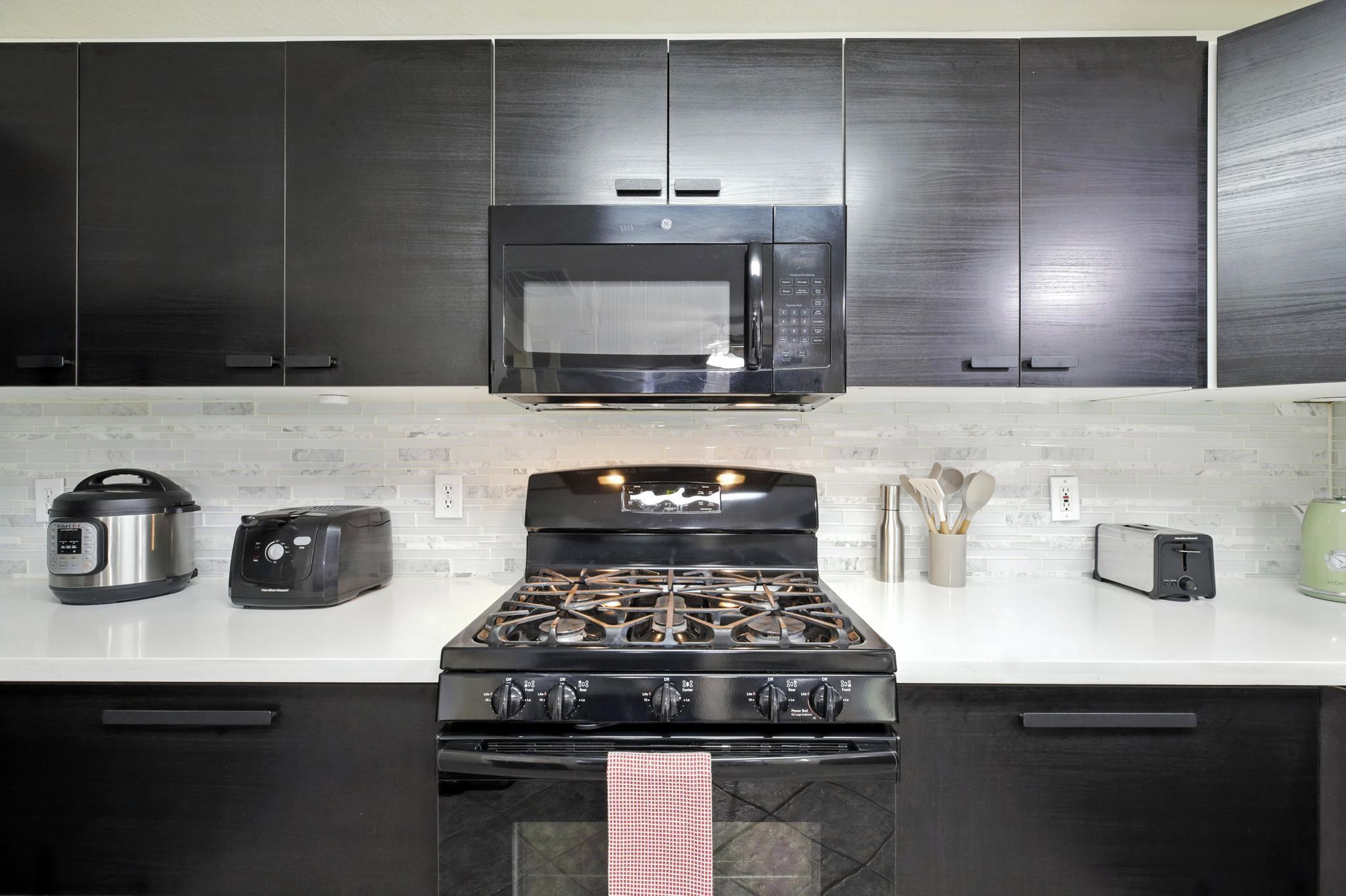 A modern kitchen with dark cabinets, a stainless steel microwave, a gas stove, a toaster, and a kettle.