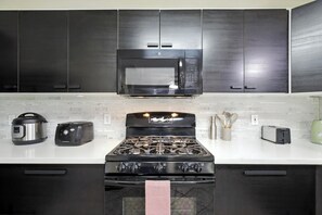 A modern kitchen with dark cabinets, a stainless steel microwave, a gas stove, a toaster, and a kettle.