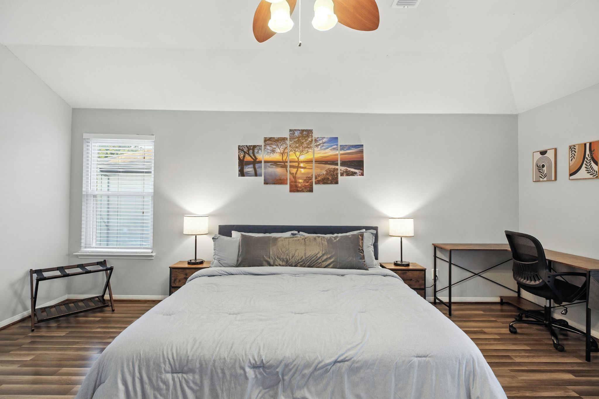 Une chambre à coucher comprenant un lit, des tables de chevet, un bureau, une chaise, une fenêtre avec des stores et une œuvre d’art accrochée au mur.