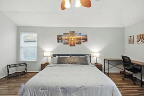 Une chambre à coucher comprenant un lit, des tables de chevet, un bureau, une chaise, une fenêtre avec des stores et une œuvre d’art accrochée au mur.
