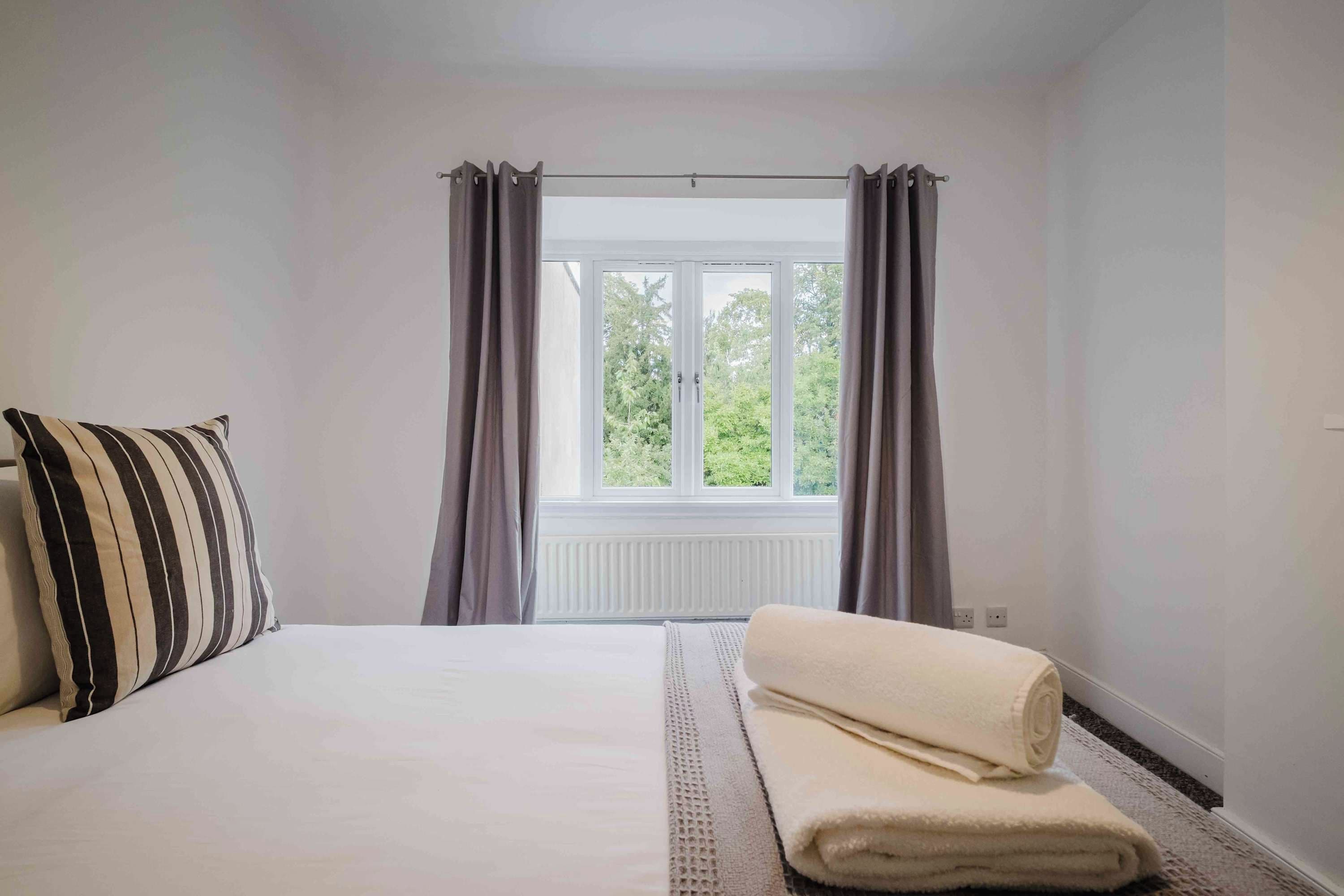 Un dormitorio con cama, ventana con cortinas y radiador.