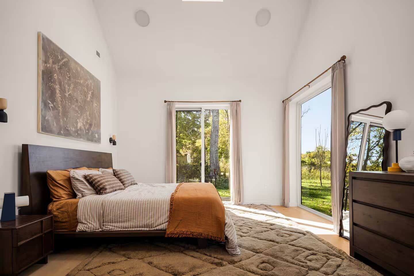 A bedroom with a bed, a dresser, a nightstand, a large window, and a view of the outdoors.