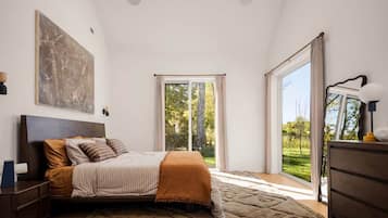 A bedroom with a bed, a dresser, a nightstand, a large window, and a view of the outdoors.