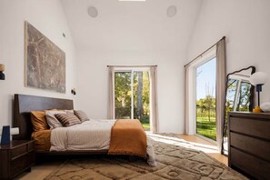 Une chambre à coucher comprenant un lit, une commode, une table de chevet, une grande fenêtre et une vue sur l’extérieur.