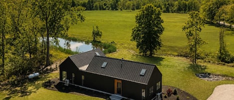 Un bâtiment moderne à deux étages, doté d’un toit en métal, entouré d’une pelouse bien entretenue et d’un petit étang.