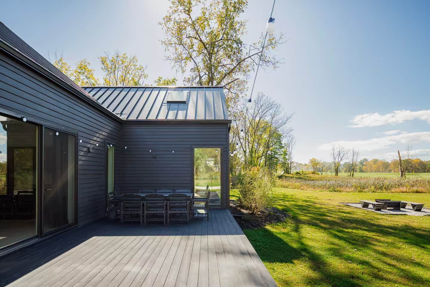 A modern house with a deck, a covered outdoor seating area, and a view of a grassy field.
