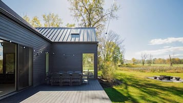 A modern house with a deck, a covered outdoor seating area, and a view of a grassy field.