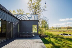 Une maison moderne dotée d’une terrasse, d’un espace salon extérieur abrité et offrant une vue sur un champ verdoyant.