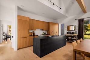 A modern kitchen with wooden cabinets, a black island, and a dining area with a table and chairs. - The Schoolhouse | Catskills Mountain Views (Saugerties)