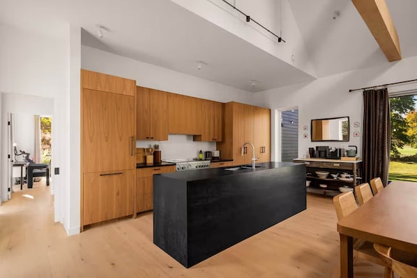 Une cuisine moderne avec des meubles en bois, un îlot central noir et un coin repas comprenant une table et des chaises.