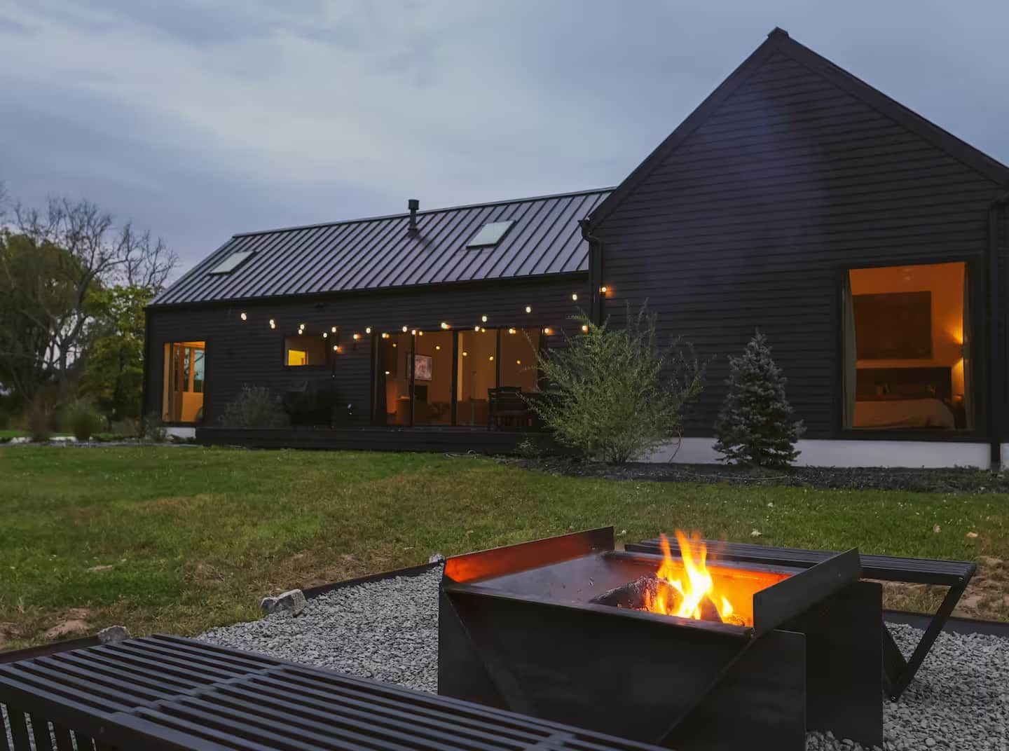 A modern house with a large deck, a fire pit, and a well-maintained lawn.