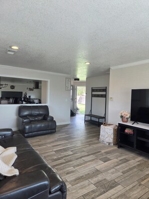 A living room with a leather sofa, a television, and a kitchen area in the background. - Charming 5-bedroom house with AC in vibrant Aurora. (Aurora)