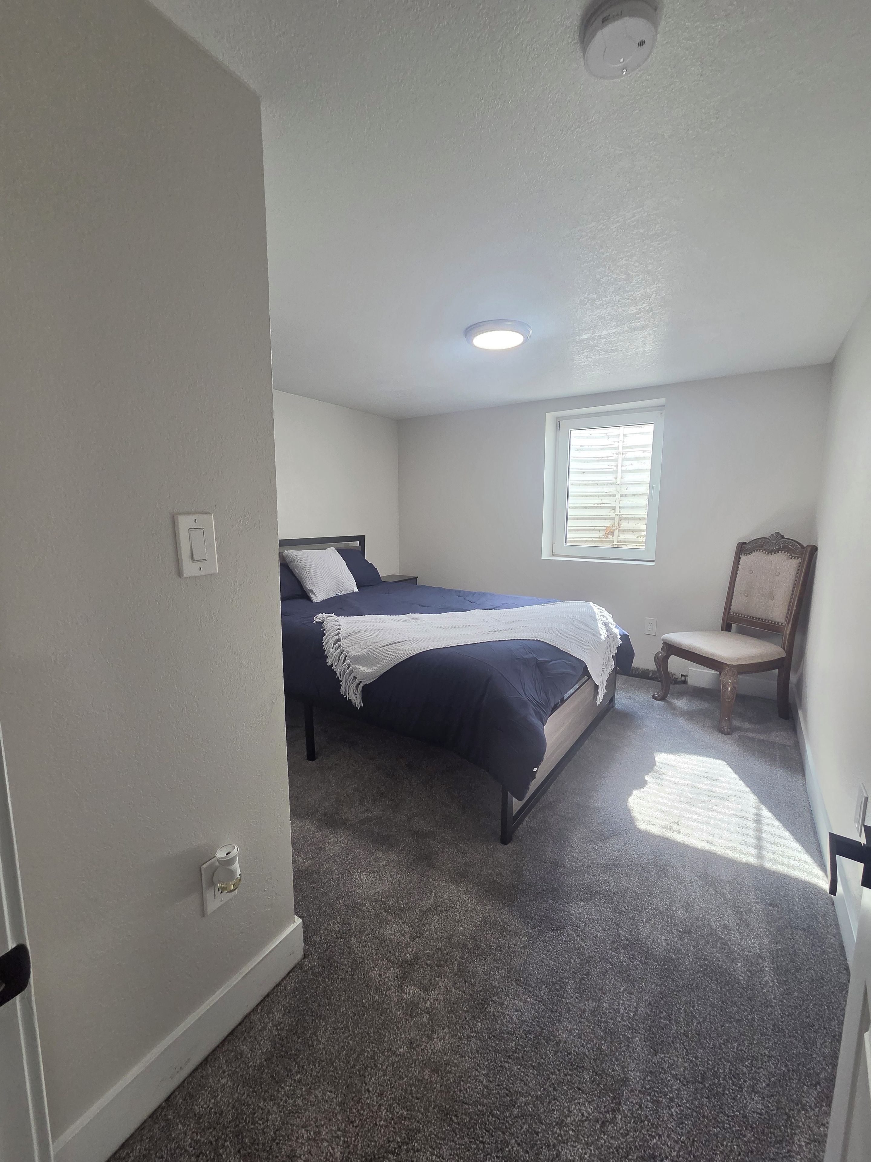 A bedroom with a bed, a chair, a window, and a ceiling light.