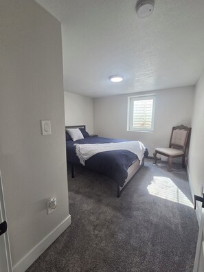 Ein Schlafzimmer mit einem Bett, einem Sessel, einem Fenster und einer Deckenleuchte.