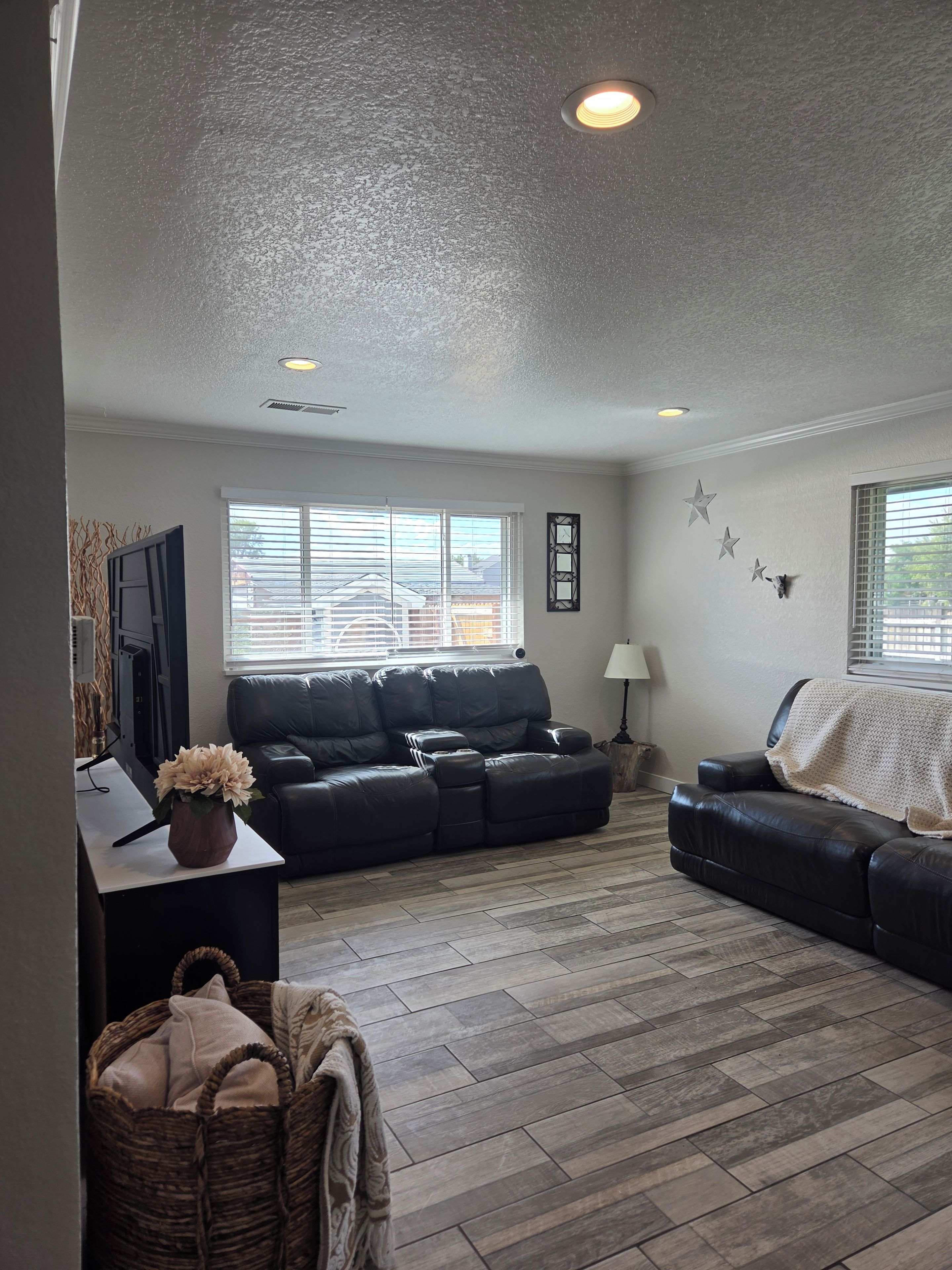A living room with a sectional sofa, a flat-screen TV, a decorative wall, and a window with blinds.