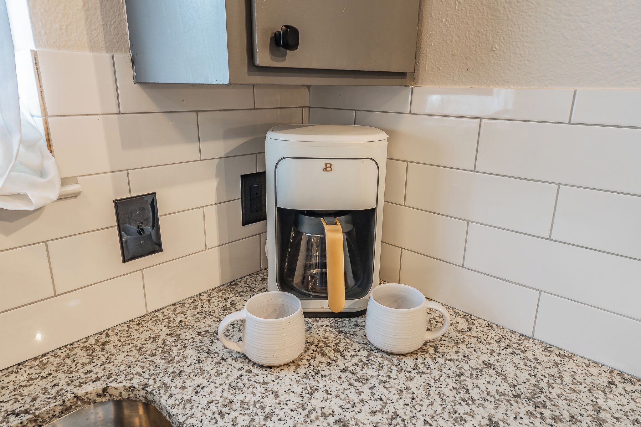 A kitchen with a coffee maker, two mugs, and a cabinet.