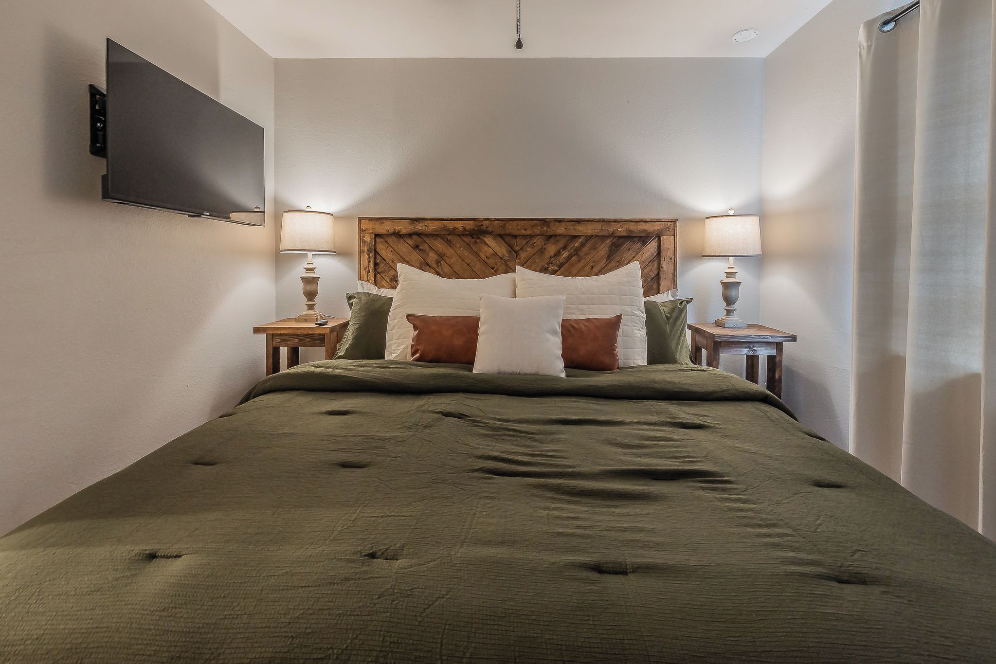 Una camera da letto con un letto, due comodini, una TV montata a parete e una testiera in legno.
