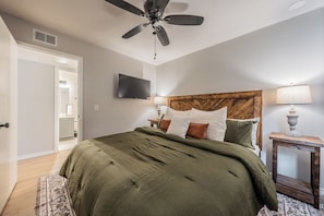 Een slaapkamer met een bed, een plafondventilator, een televisie en een houten hoofdeinde.