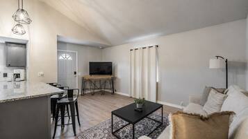 A modern living room with a kitchen area, a dining table, and a TV.