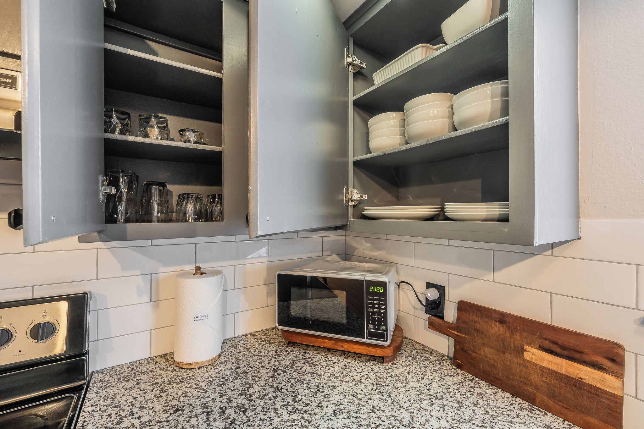 Une cuisine équipée d’un four à micro-ondes, d’une planche à découper en bois et d’un meuble contenant de la vaisselle et des verres.