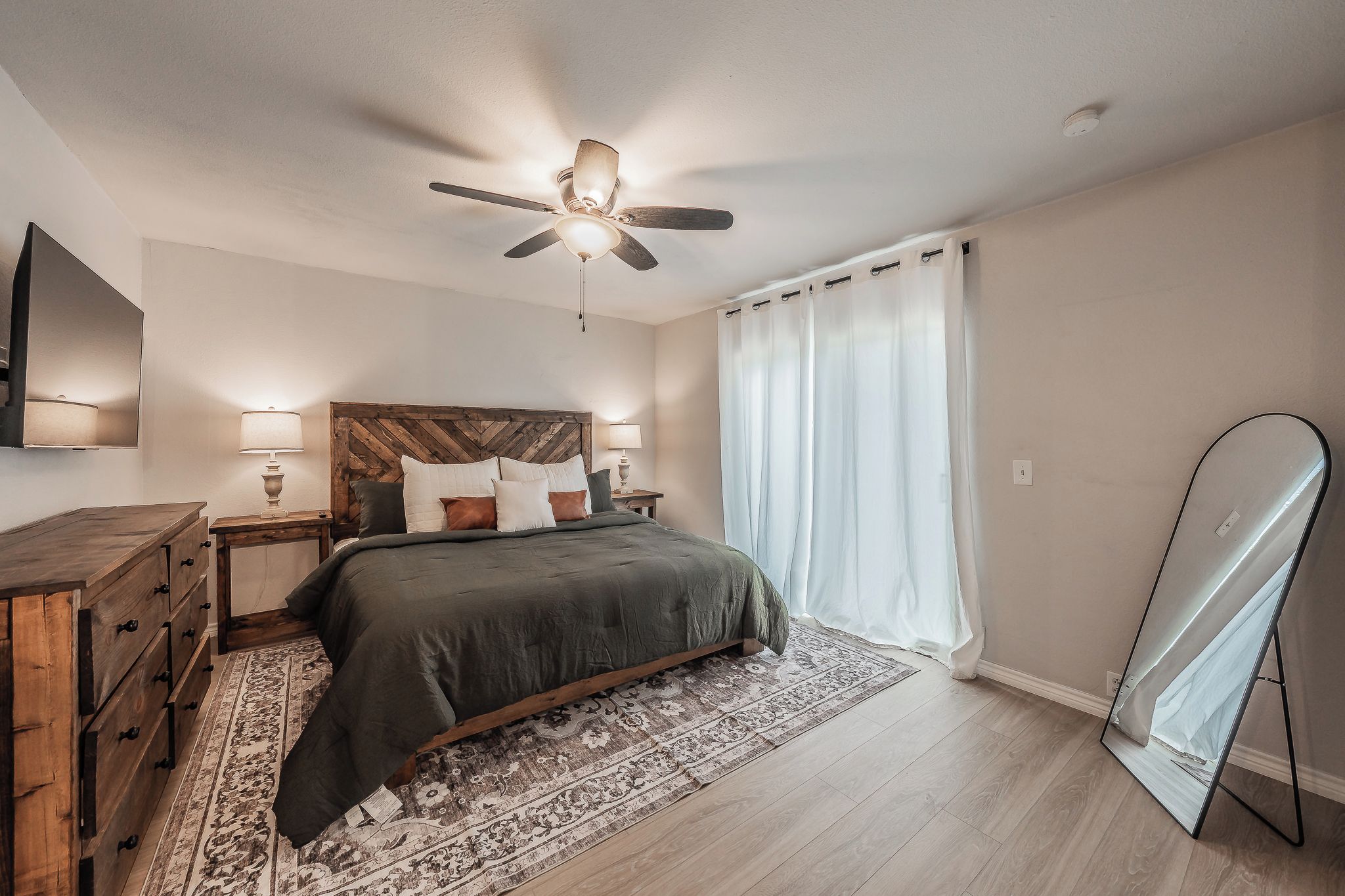 A bedroom with a bed, nightstands, a ceiling fan, a TV, and a large mirror.
