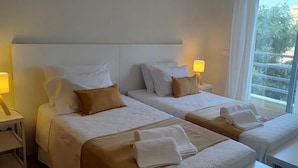 Une chambre d’hôtel avec deux lits, chacun équipé d’un oreiller, d’une lampe de chevet et d’une fenêtre donnant sur un paysage agréable.