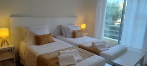 Ein Hotelzimmer mit zwei Betten, jeweils mit Kissen, einer Nachttischlampe und einem Fenster mit Blick.