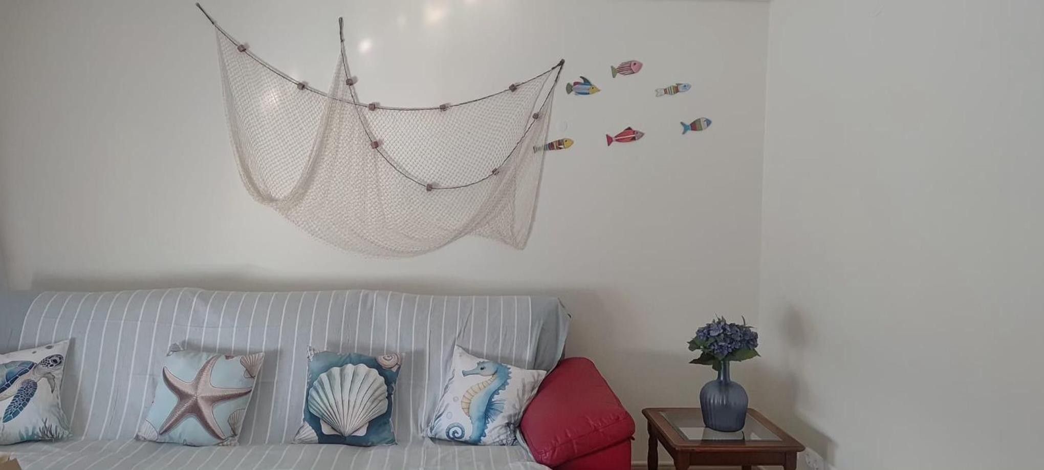 Una habitación con un sofá a rayas, almohadones decorativos, una mosquitera colgante y un jarrón sobre una mesita de noche.