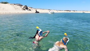 Deux personnes font de la plongée avec tuba dans une eau claire, avec une plage et un bateau en arrière-plan.