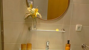 Une salle de bain avec un meuble-lavabo foncé, un miroir rond, un lavabo en verre et un tapis de bain jaune.