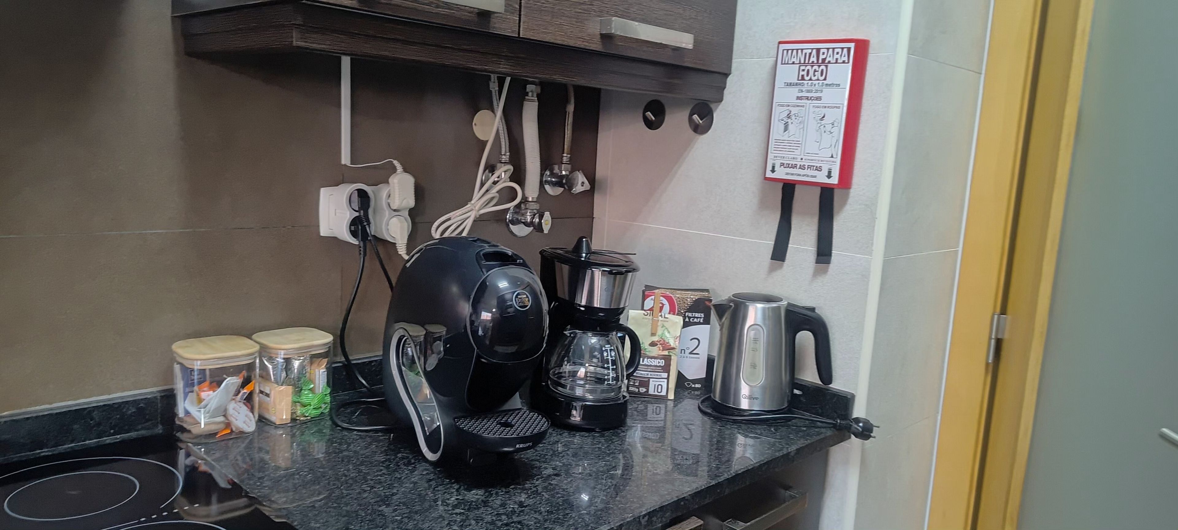 A kitchen with a coffee maker, kettle, and various kitchen utensils on the counter.