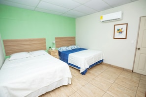 Ein Hotelzimmer mit zwei Betten, einem Nachttisch, einer Wand-Klimaanlage und einem gerahmten Bild.