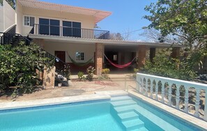 Ein zweistöckiges Haus mit Swimmingpool, Hängematte und Balkon.