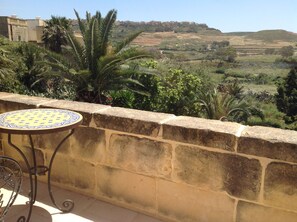 A balcony with a table and chairs, overlooking a hilly landscape with buildings in the distance. - Nostalgia suite at Dar Tal Kaptan, Ghasri, Gozo. Victorian themed room (Ghasri)