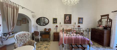 A bedroom with a bed, a chair, a desk, a dresser, a mirror, and a chandelier.