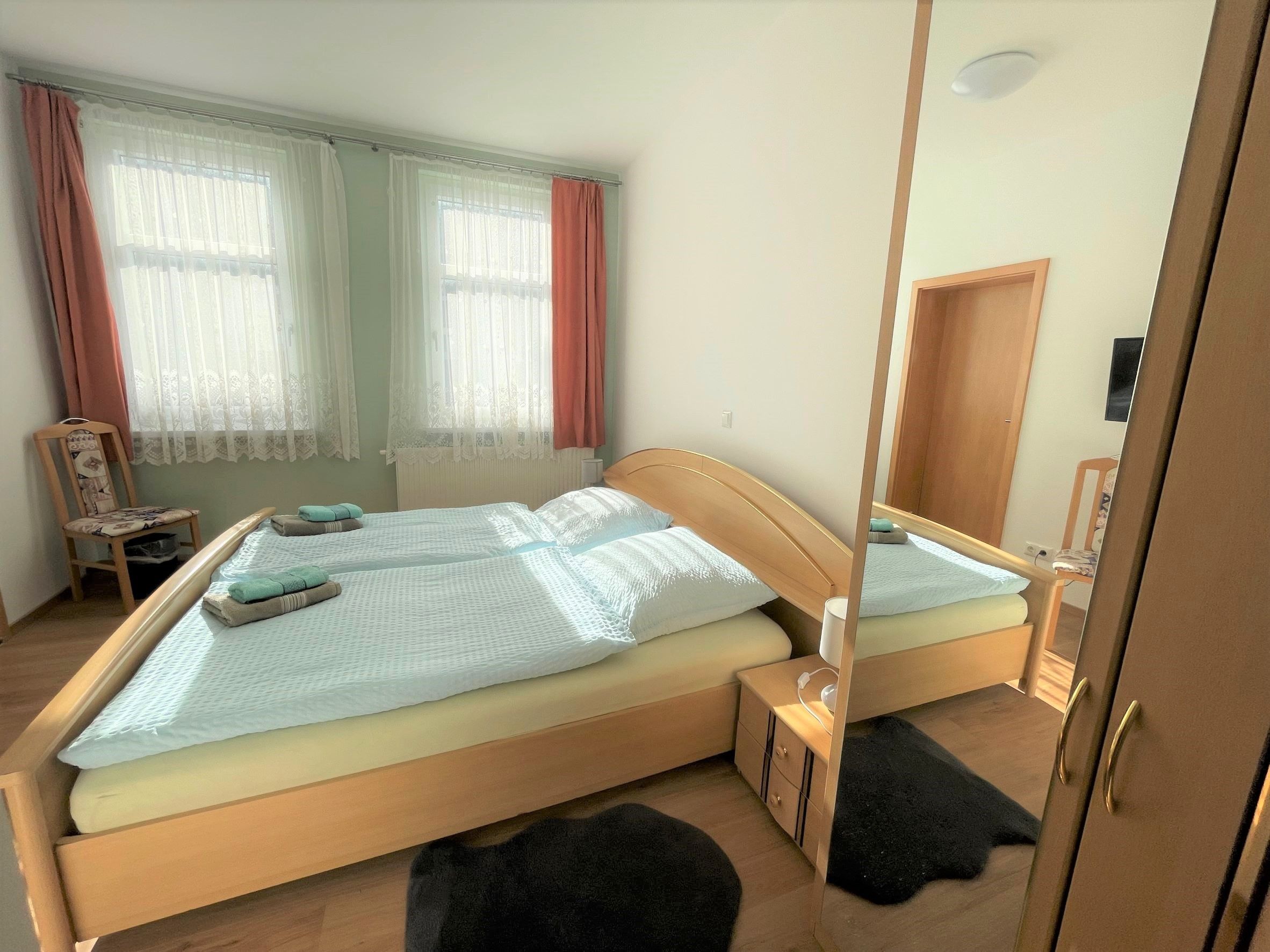 A double bed with a wooden frame, a bedside table, a chair, and a window with curtains.