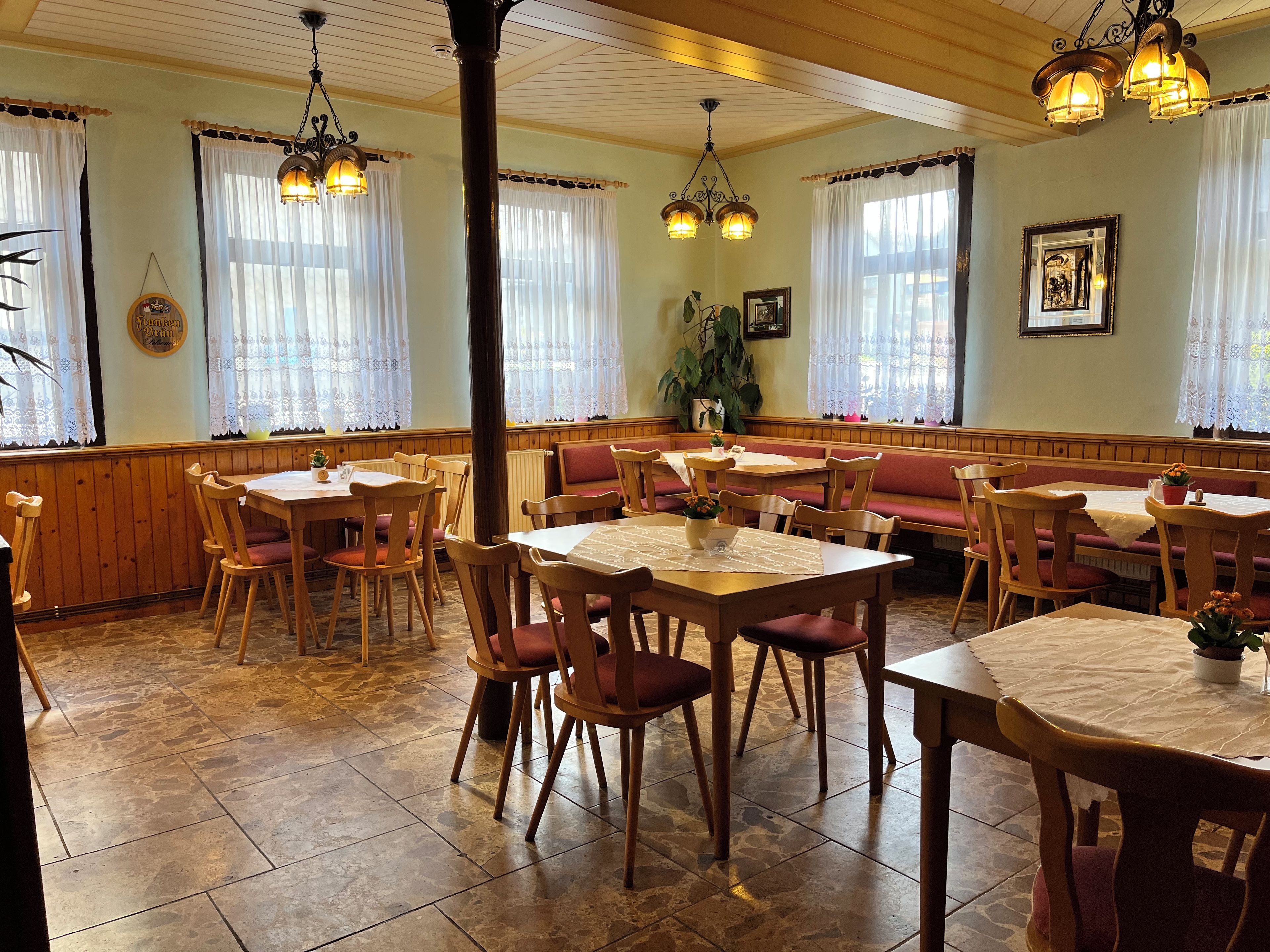 A restaurant with wooden tables and chairs, a stone-tiled floor, and hanging light fixtures.