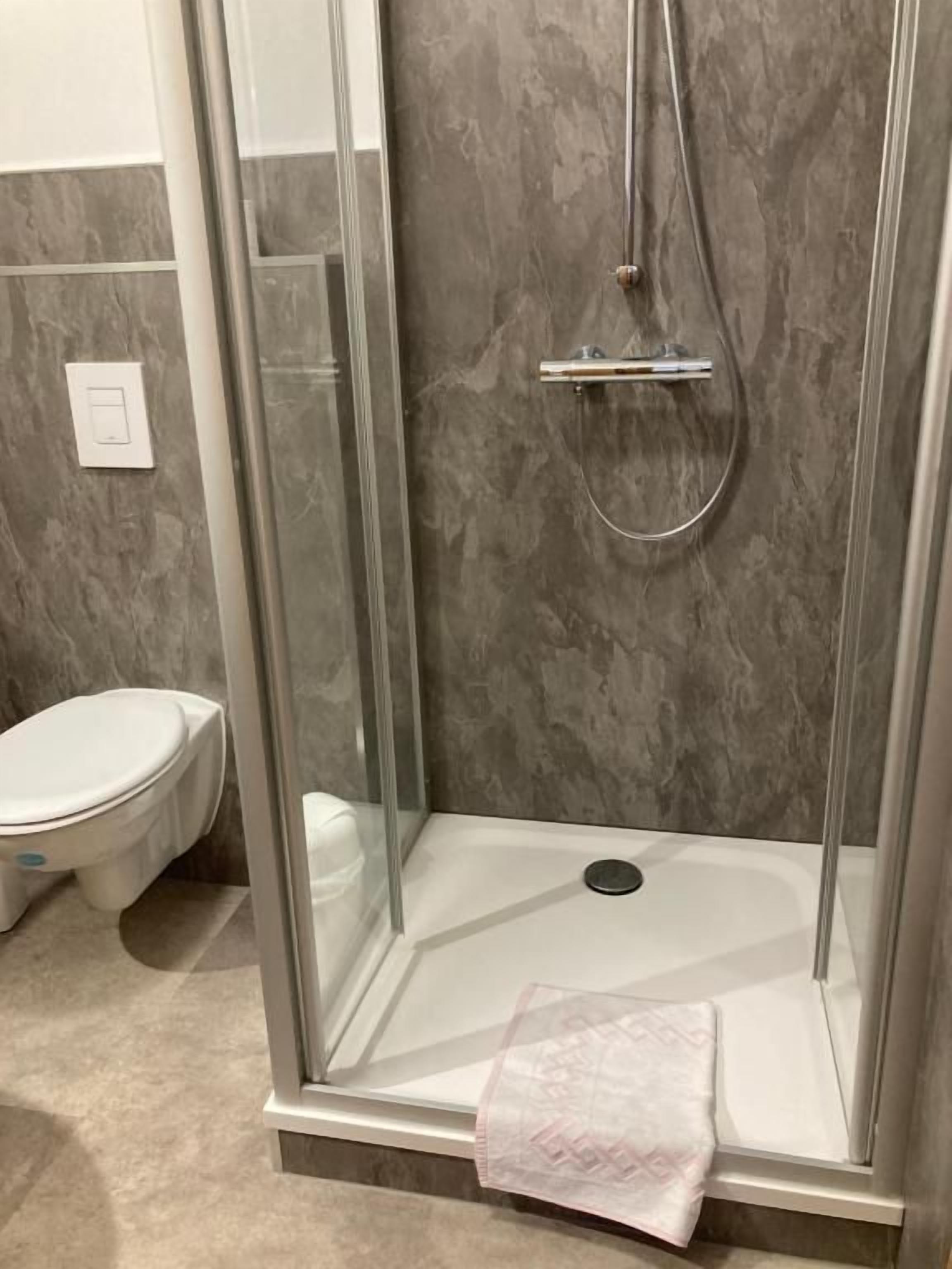 Een douchecabine met een glazen deur, een wit toilet en een marmeren wand.
